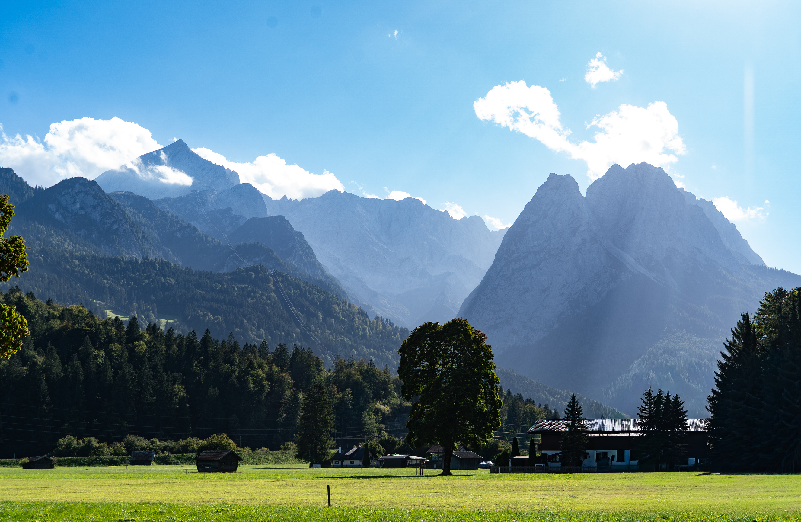 Berglandschaft bei Garmisch-Partenkirchen mit grüner Wiese und bewaldeten Hängen.