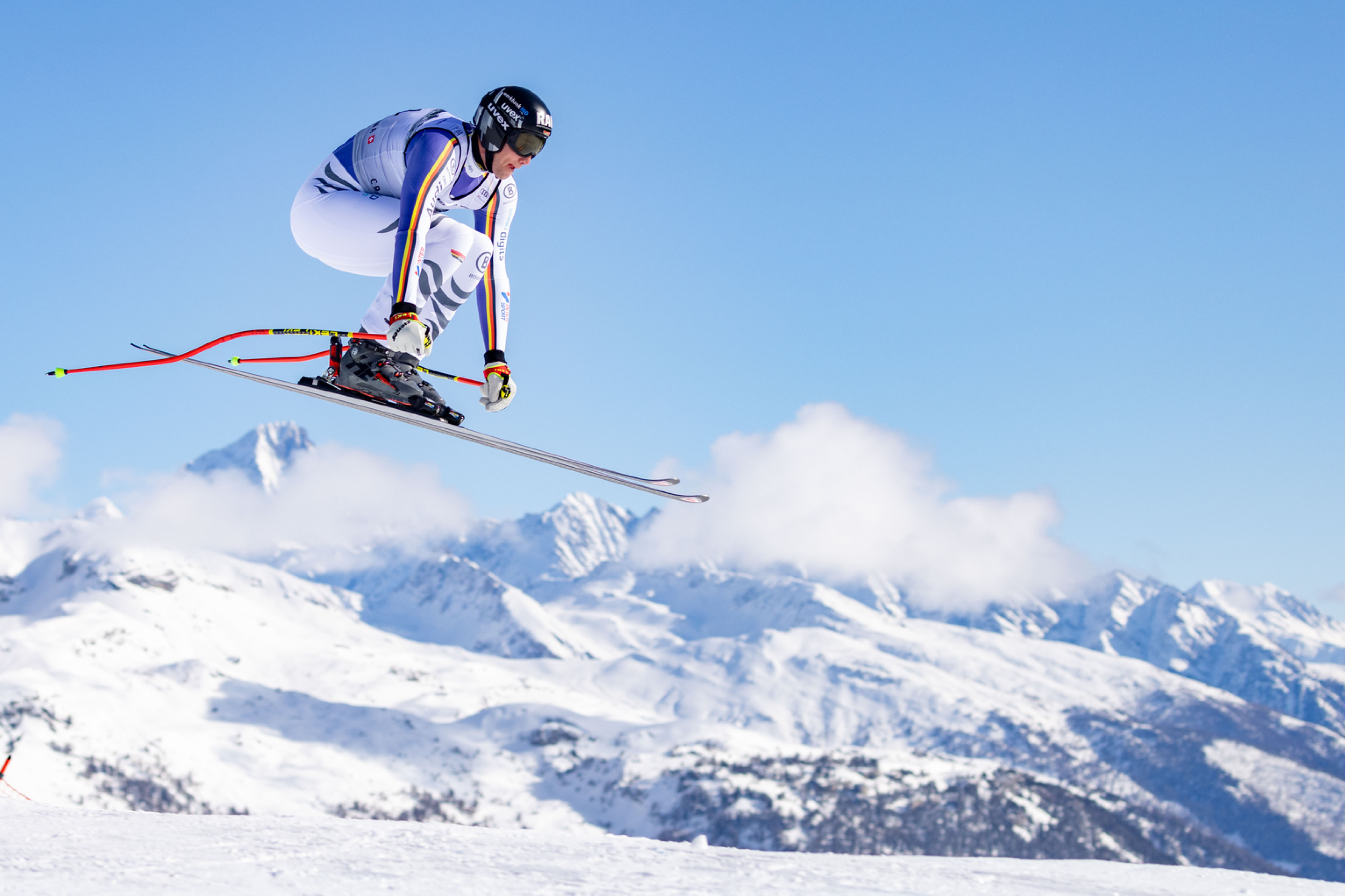 Skifahrerin Katharina Liensberger fährt in rasanter Abfahrt um eine rote Stange, trägt Schutzhelm und Skianzug, schneebedeckte Piste, bewaldete Umgebung im Hintergrund. Text auf Kleidung: "RAU", "WÜRTH".