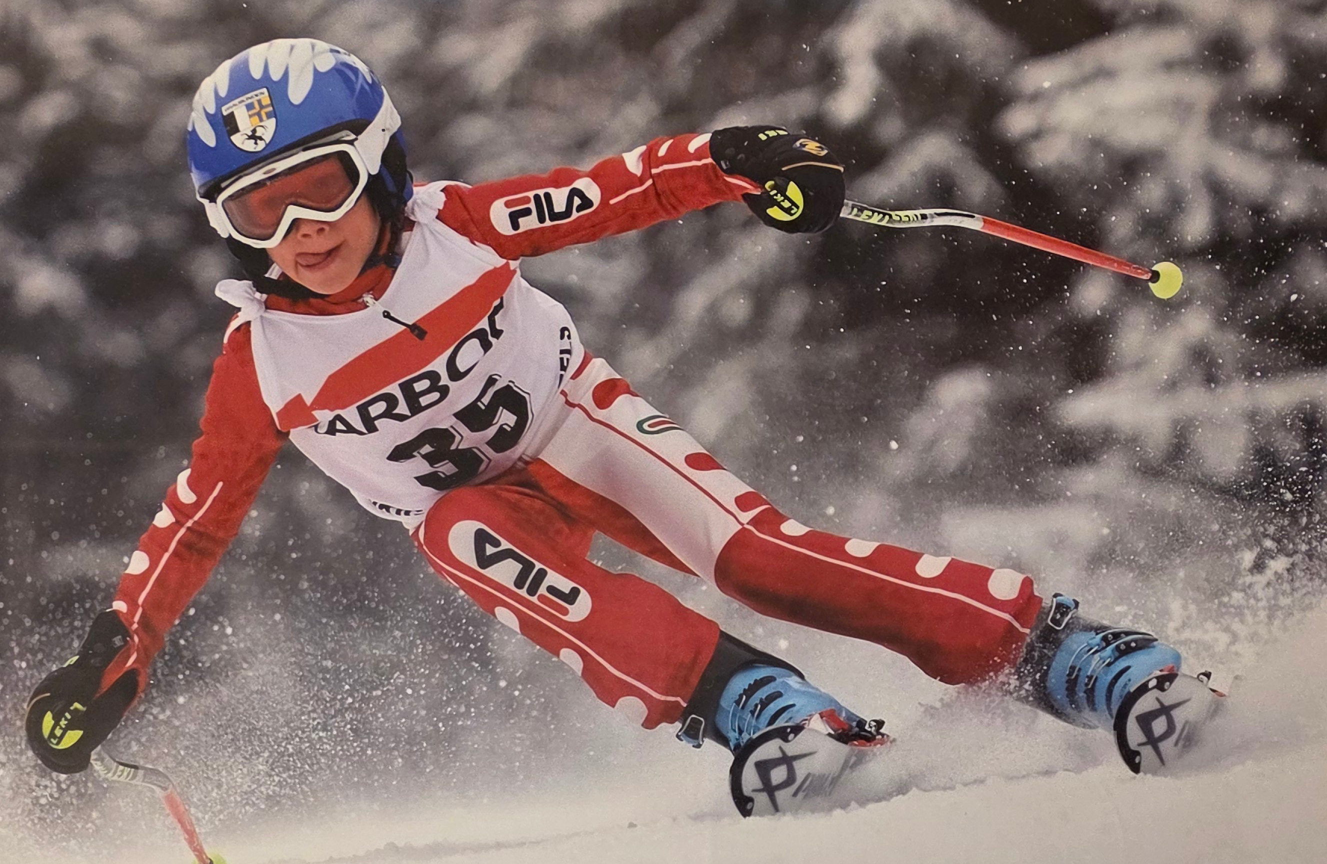 Junger Skirennfahrer Luis Vogt in rot-weißem Rennanzug fährt dynamisch durch eine Kurve und wirbelt dabei Schnee auf.